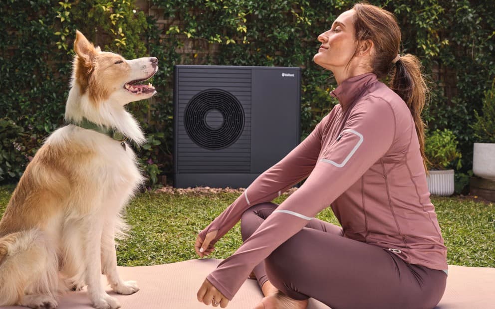 Hund und Frau sitzen vor Wärmepumpe auf Yogamatte.